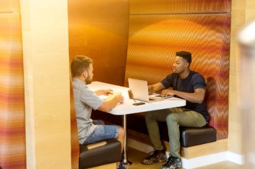 2 people sitting in a booth with a laptop